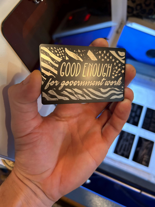 Hand holding a card with 'Good Enough for Government Work' text in front of a computer keyboard.