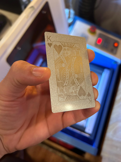 Hand holding a silver on silver playing card with a King of Hearts laser engraving in front of a machine in the background