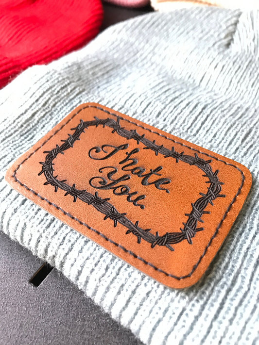 Leather patch with 'I hate you' text on a textured beanie threaded surface