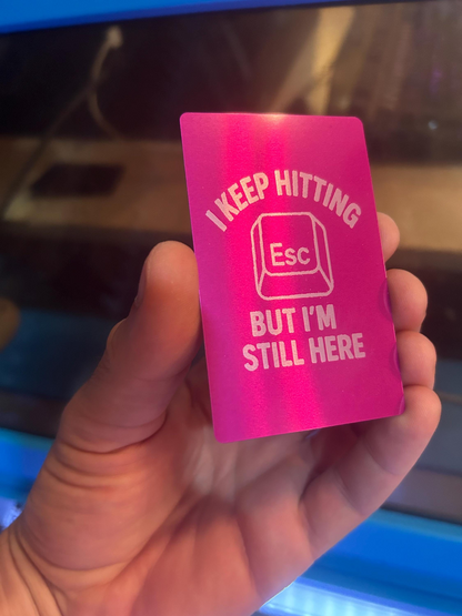 Purple and silver laser engraved metal gag gift placard with text 'I keep hitting Esc but I'm still here' held in a hand.