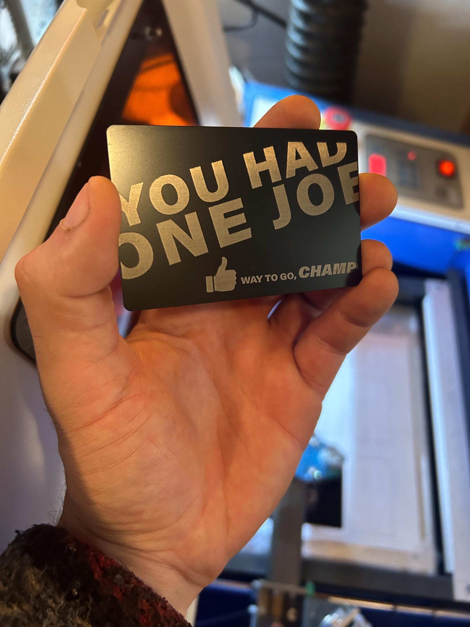 Hand holding a card with text 'YOU HAD ONE JOB WAY TO GO, CHAMP' in front of a machine.