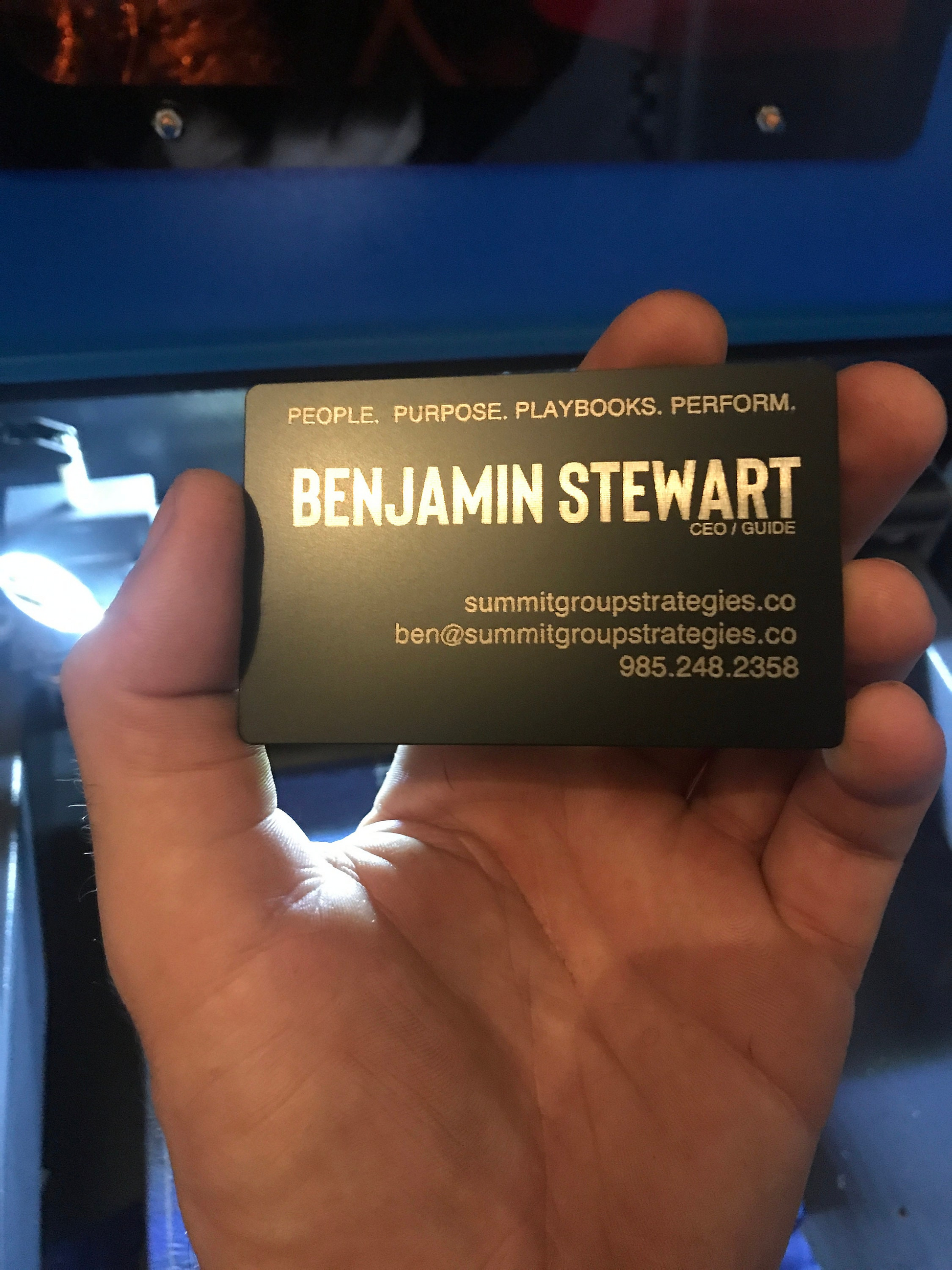 Hand holding a custom metal laser engraved business card with name, tagline and contact information.