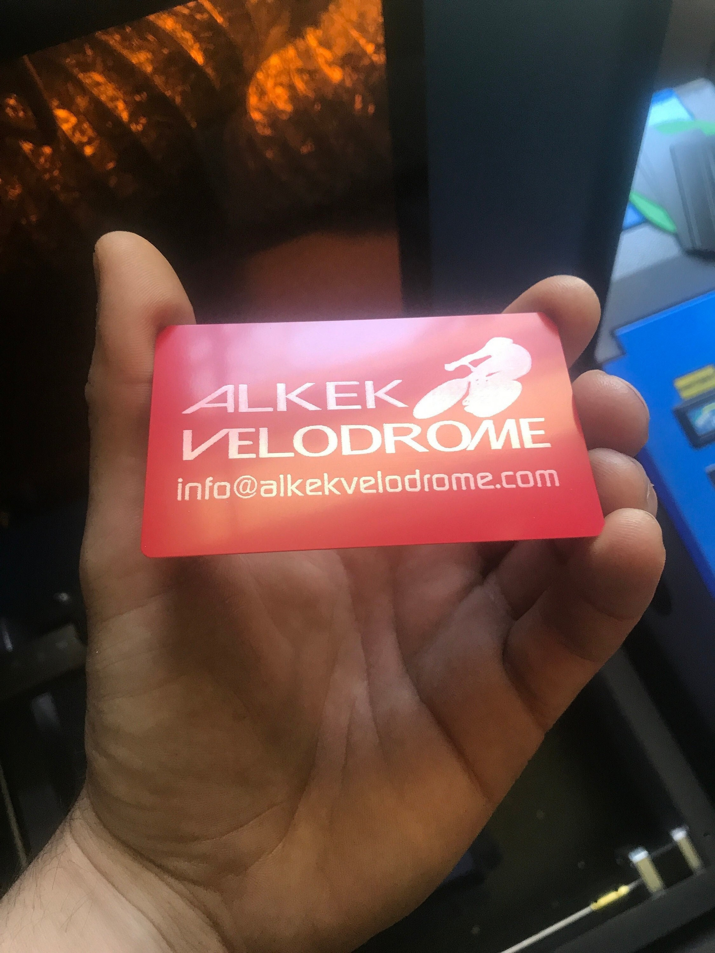 Hand holding a red and silver metal business card with 'Velodrome' branding and customized contact information.