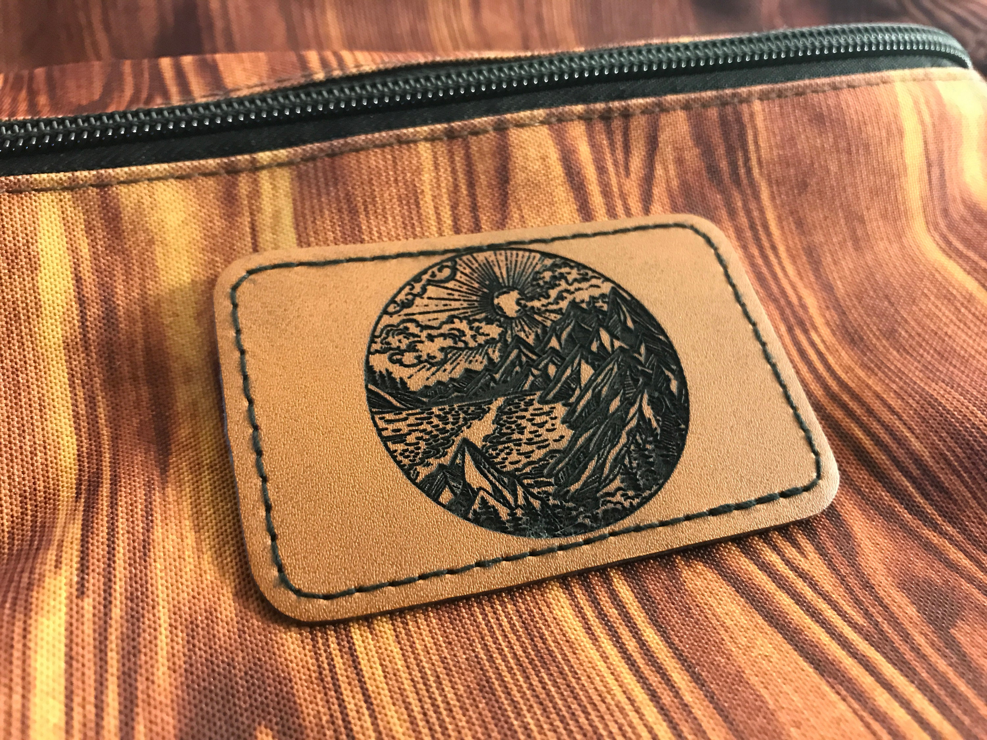 Brown leather patch with leather burned nature mountain and sunshine clouds design on a wooden surface