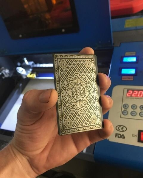 Hand holding a black and silver metal playing card in front of a cnc machine 