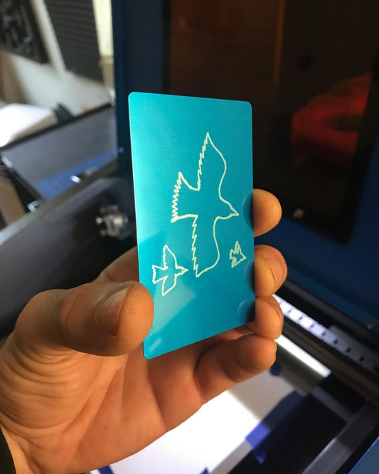 Hand holding a blue/silver laser engraved metal keepsake gift, with hand drawn bird design converted to cnc etching