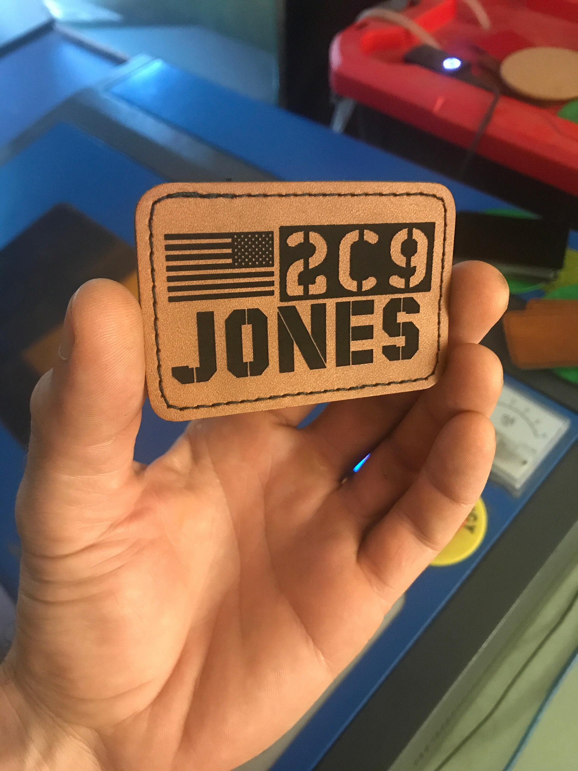 Hand holding a leather patch with personalized military identification text and American flag design engraving.