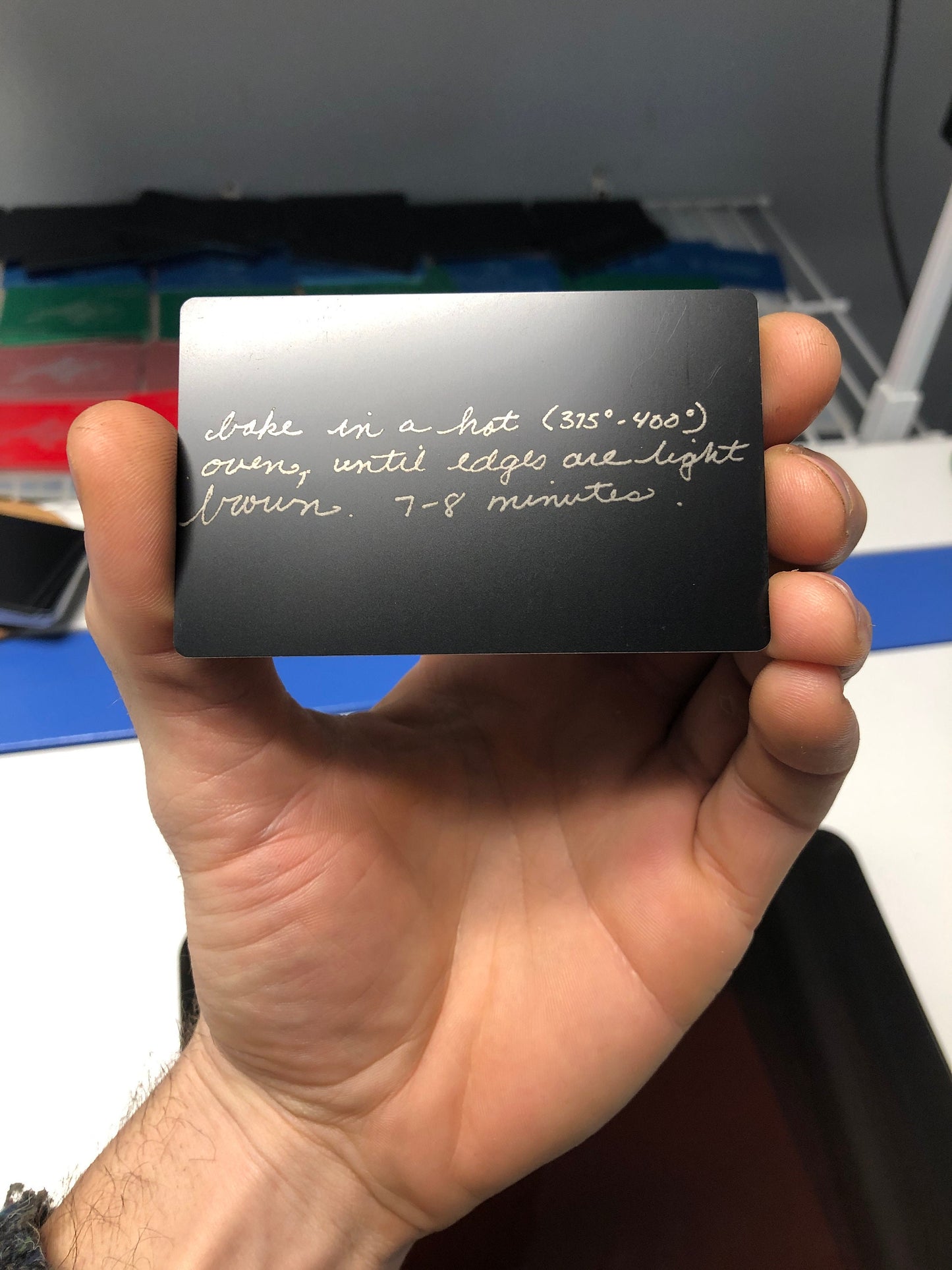 hand holding a custom metal baking instructions, with artwork taken from a sentimental note engraved on a matte black/silver card