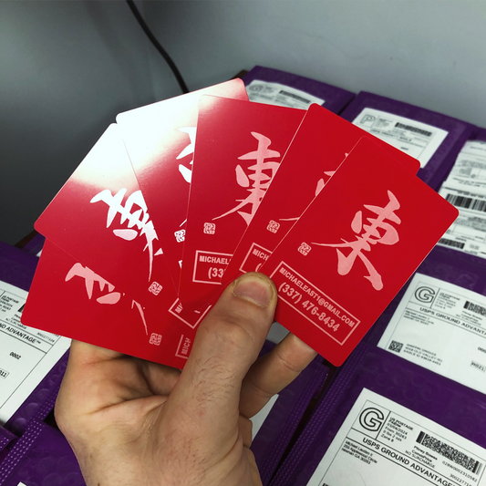Hand holding a set of red/silver metal business cards with japanese kanji characters and customized contact information in front of rows of product mailers