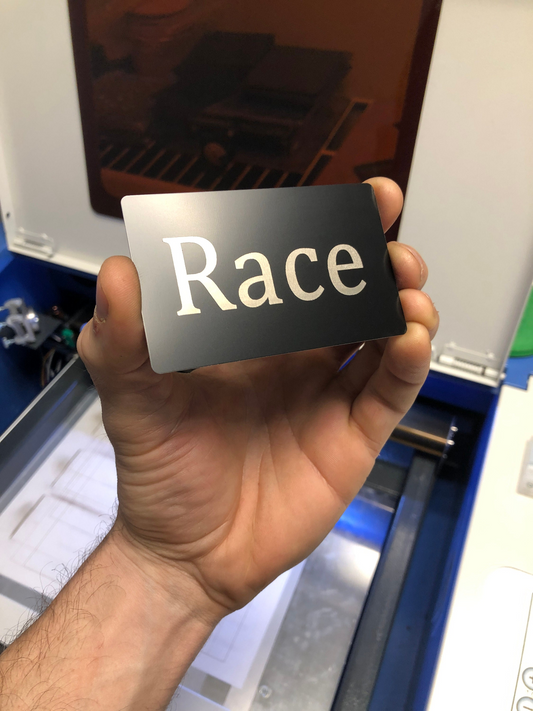 Hand holding a black metal card with the word 'Race' on it against a blurred background