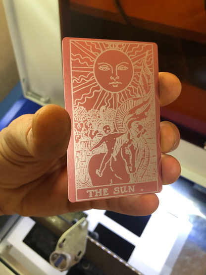 Rose gold/silver card with a sun design and 'The Sun' tarot design held by a hand.