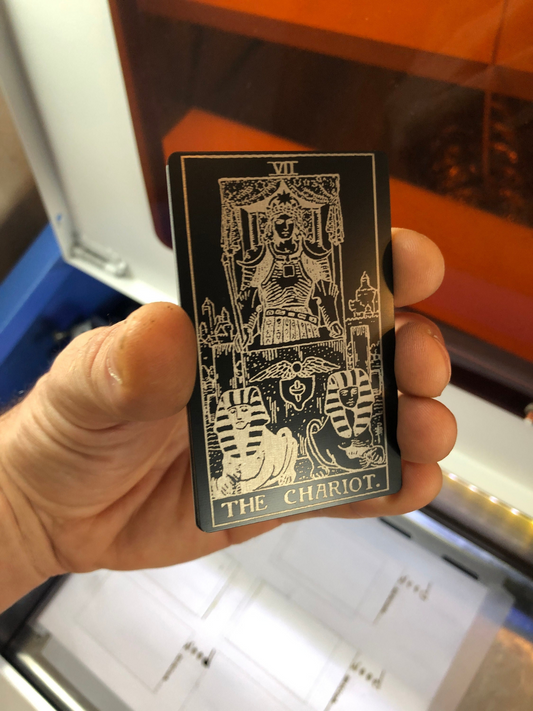 Hand holding a metal business card with tarot card design of 'The Chariot' design against a blurred background