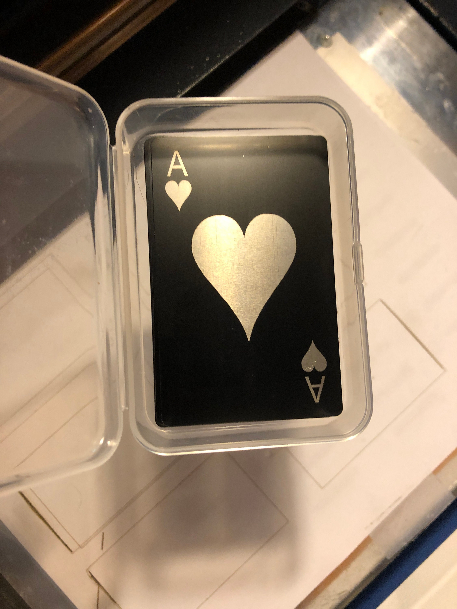 Metal playing card with ace of hearts symbol in a clear plastic case on a white surface.