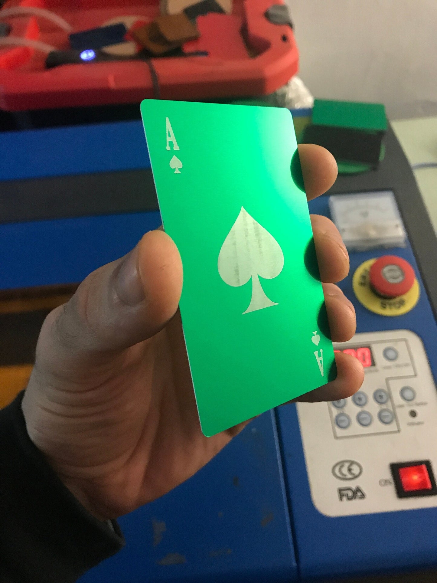 A hand holding a green anodized aluminum card with the Ace of Spades design, featuring a green and silver finish and engraved detailing.