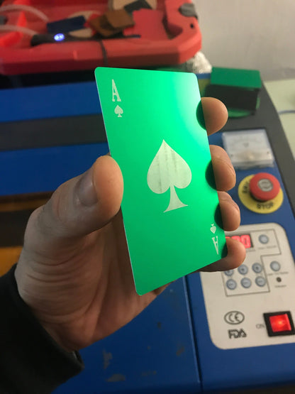 A hand holding a green anodized aluminum card with the Ace of Spades design, featuring a green and silver finish and engraved detailing.