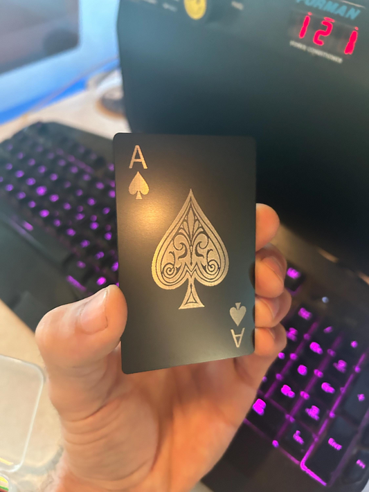 Hand holding a metal poker card with silver ace of spades design in front of a computer keyboard.