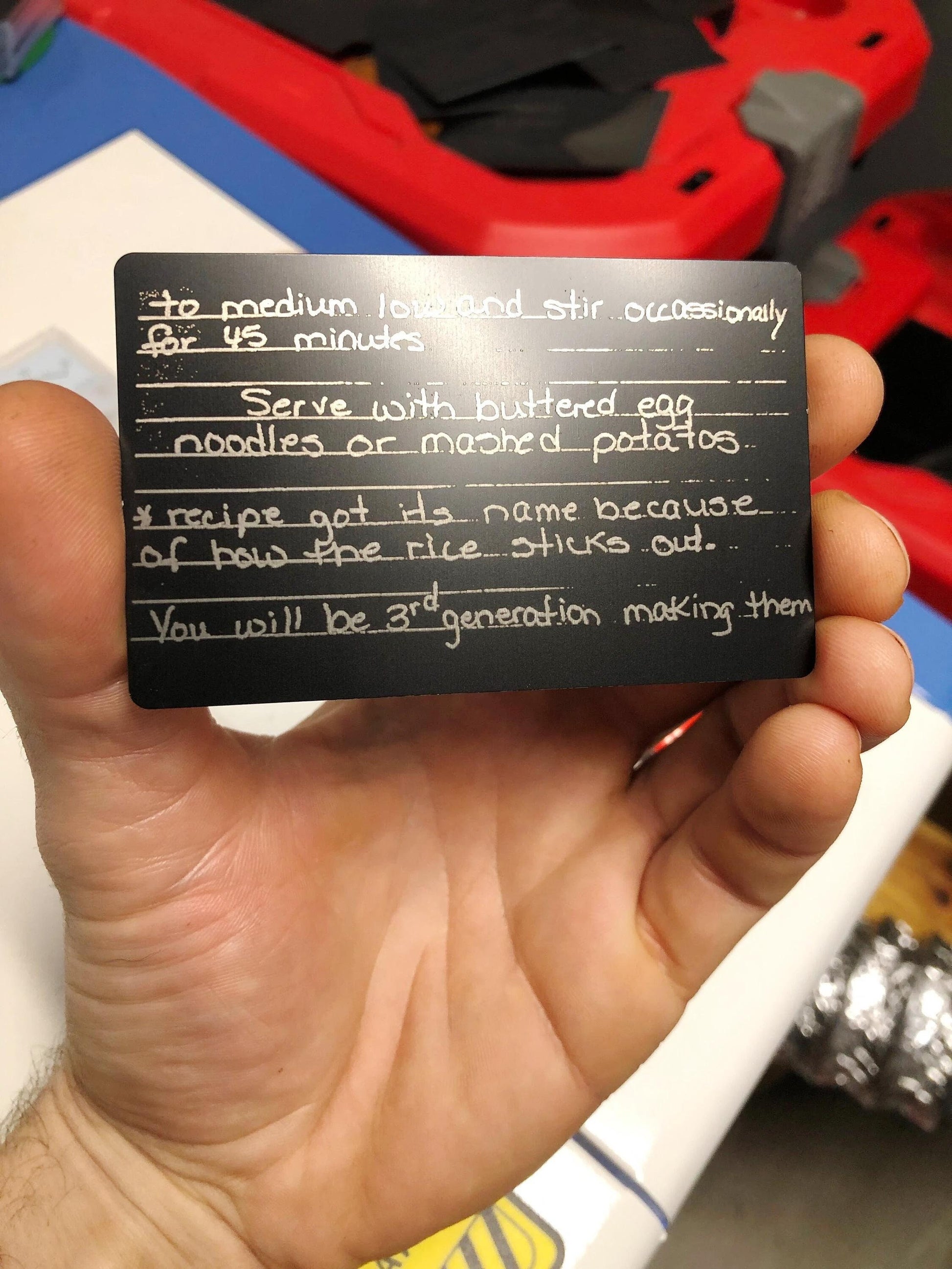 hand holding an anodized aluminum card with personalized handwriting engraved showcasing a family recipe card in front an industrial background