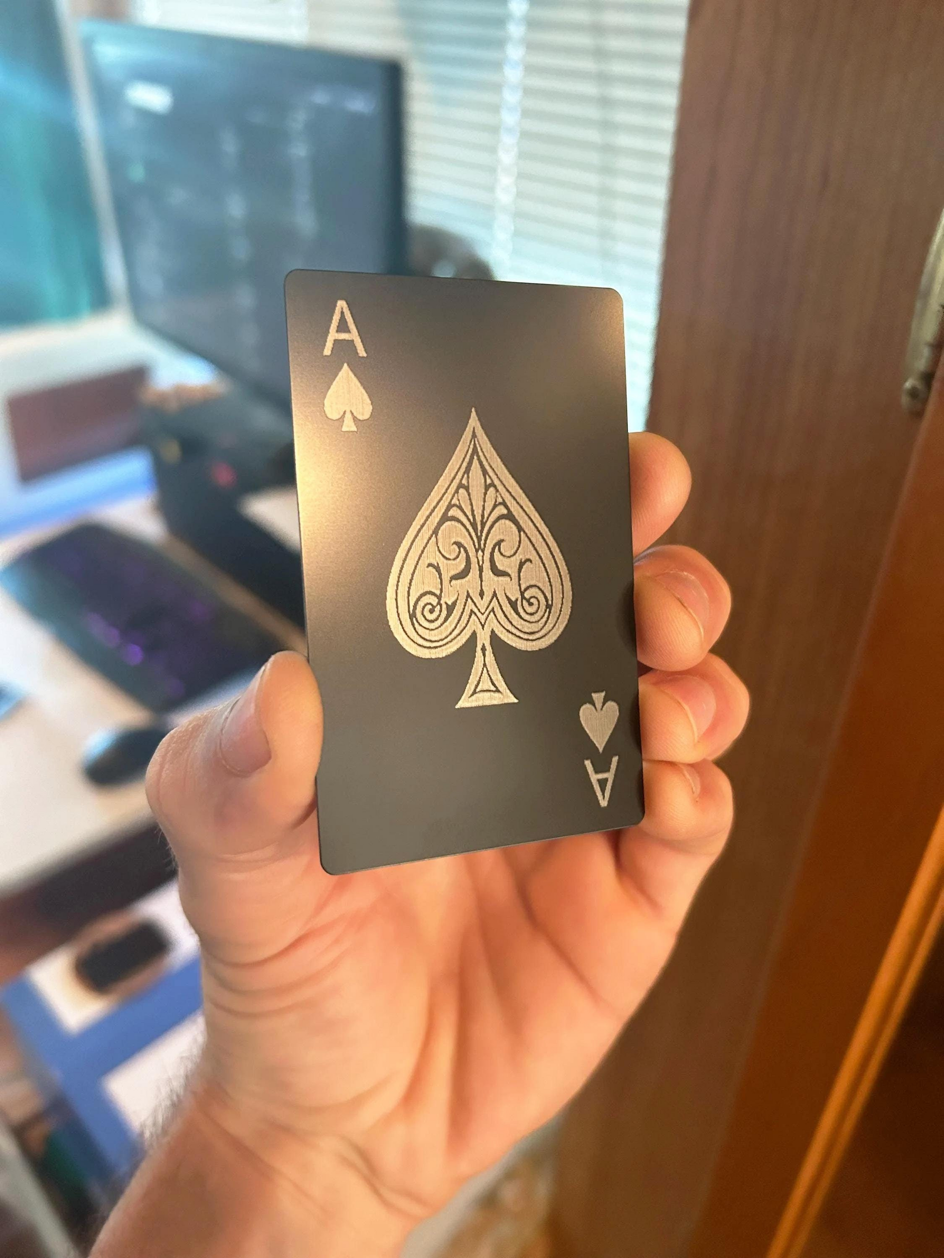 Hand holding a metal black playing card with a silver ace of spades design.