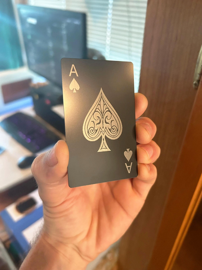 Hand holding a metal black playing card with a silver ace of spades design.