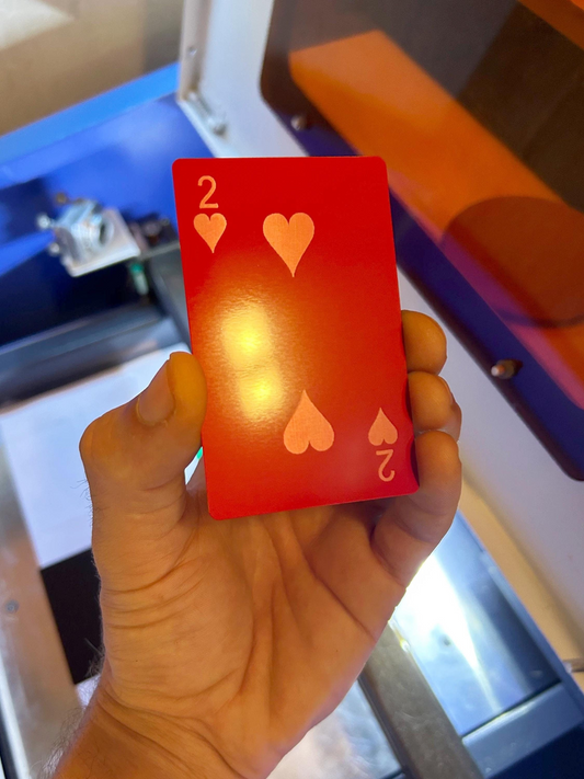 Hand holding a red metal playing card with hearts and number 2 in front of a blurred background