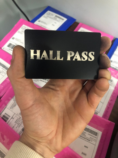 Hand holding a black metal 'HALL PASS' card with colorful background