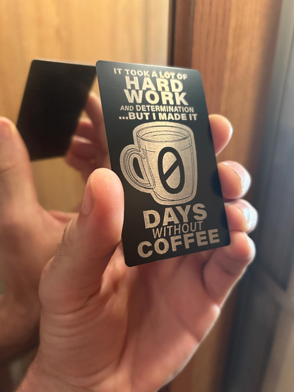 Card with '0 Days Without Coffee' text held by a person against a neutral background
