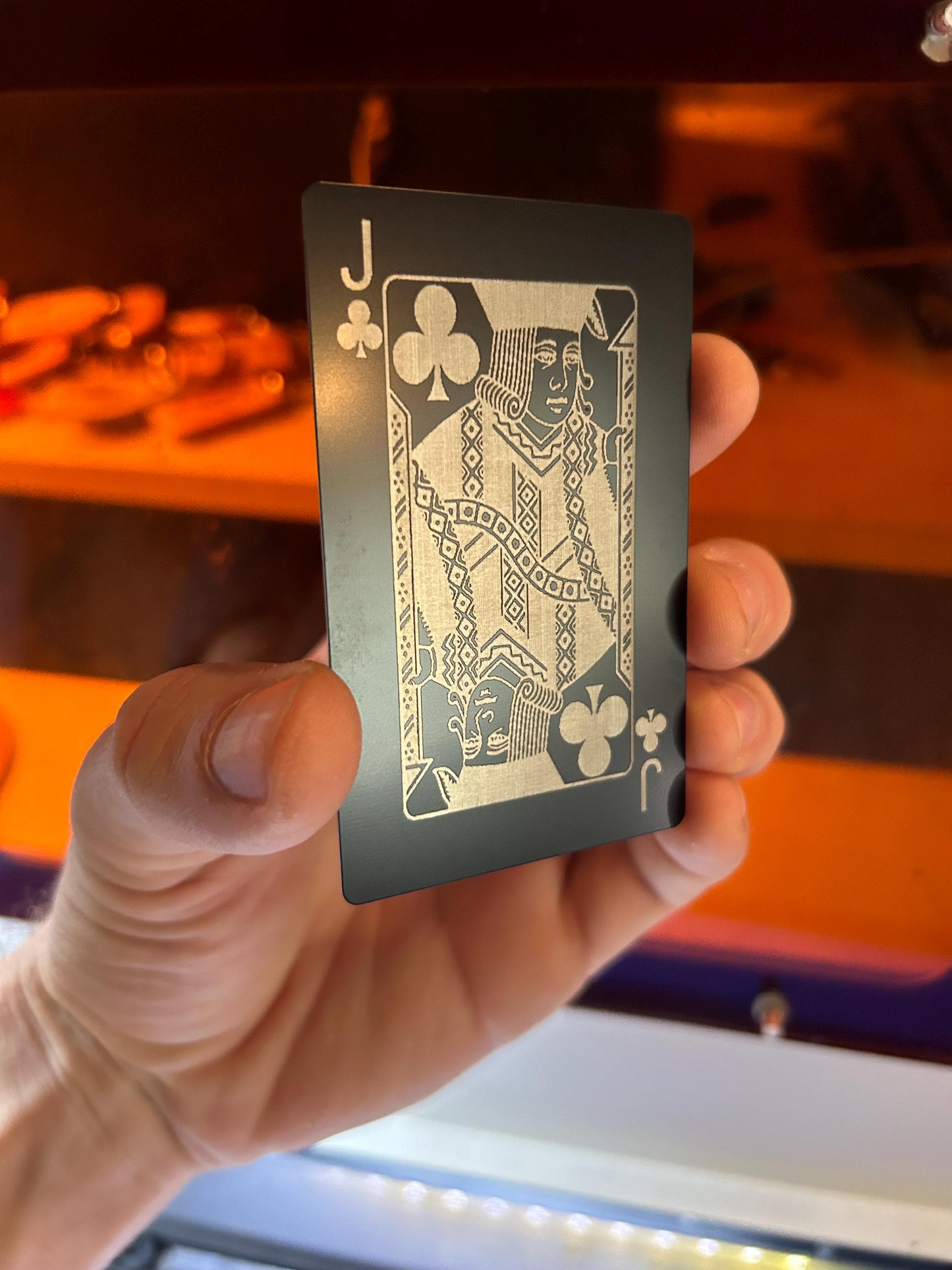 Hand holding a black and silver metal poker card with a blurred background