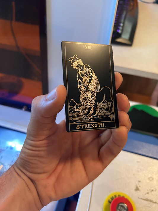 Hand holding a metal tarot card with 'Strength' at the bottom