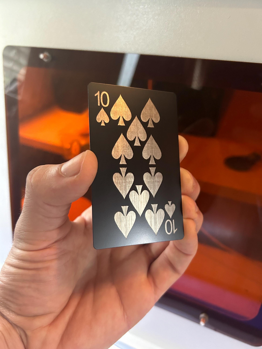 Hand holding a black metal playing card with a laser engraved design, etched into Anodized Aluminum