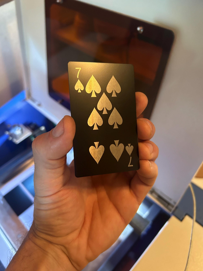 Hand holding a laser engraved metal playing card with seven of spades symbols in anodized aluminum
