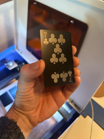 hand holding metal decorative 7 of clubs lucky number poker card in front of a machine