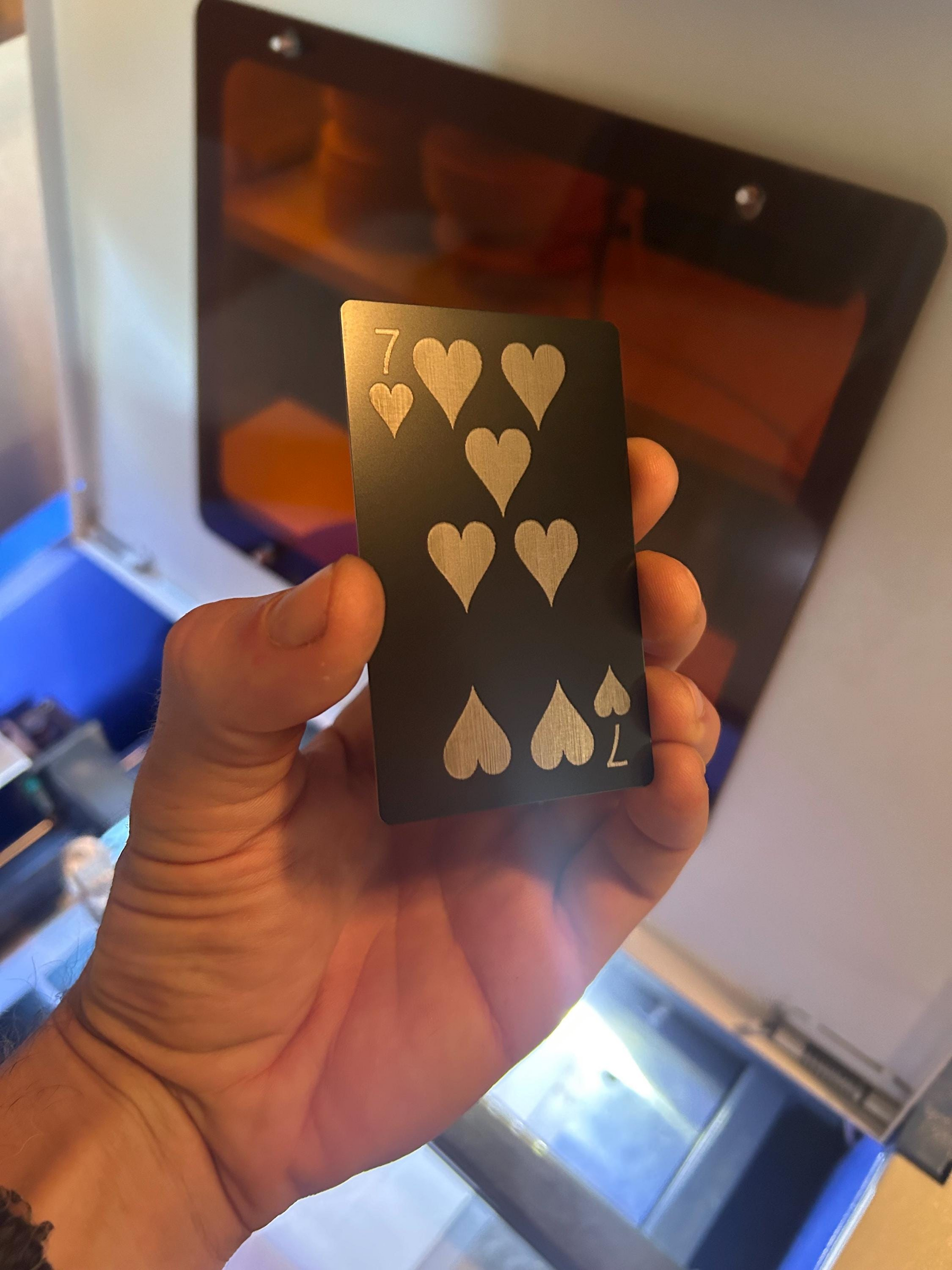 Hand holding a metal silver and black playing card with seven of hearts design against a blurred indoor background
