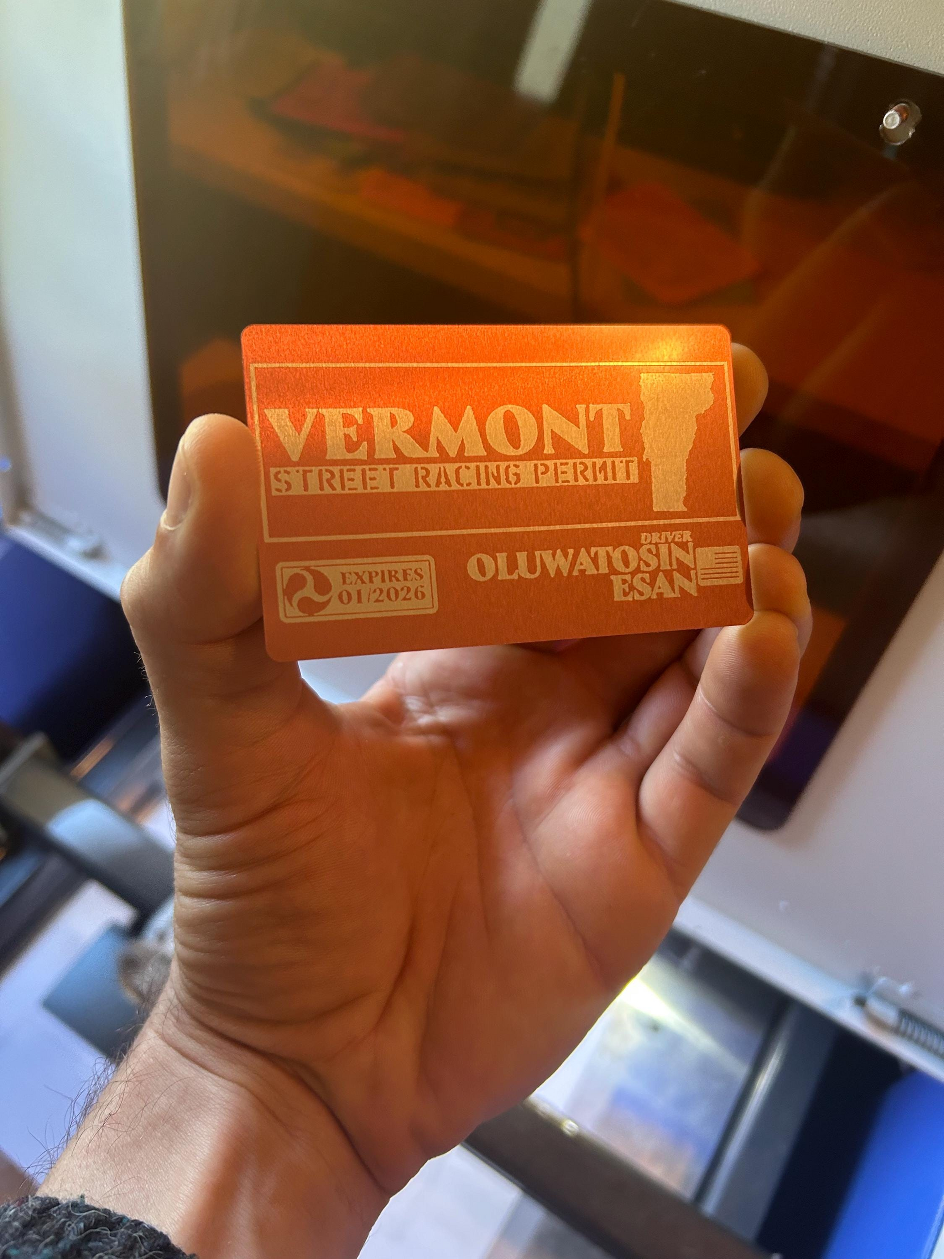 Hand holding a rose gold and silver laser engraved Vermont street racing permit card with a blurred background