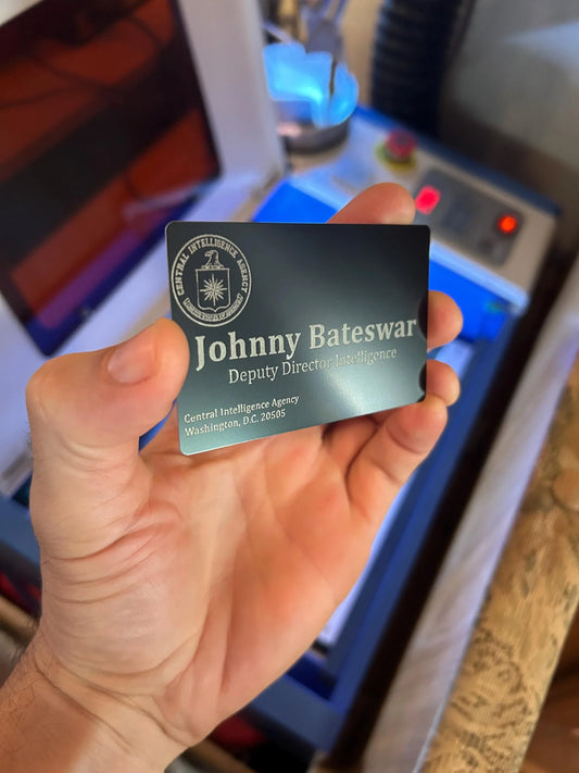 Hand holding a business card with 'Johnny Bateswar' and 'Deputy Directives Intelligence' text.