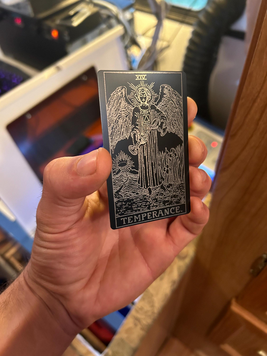 Hand holding a metal tarot wallet card titled 'Temperance' in front of a blurred indoor background.
