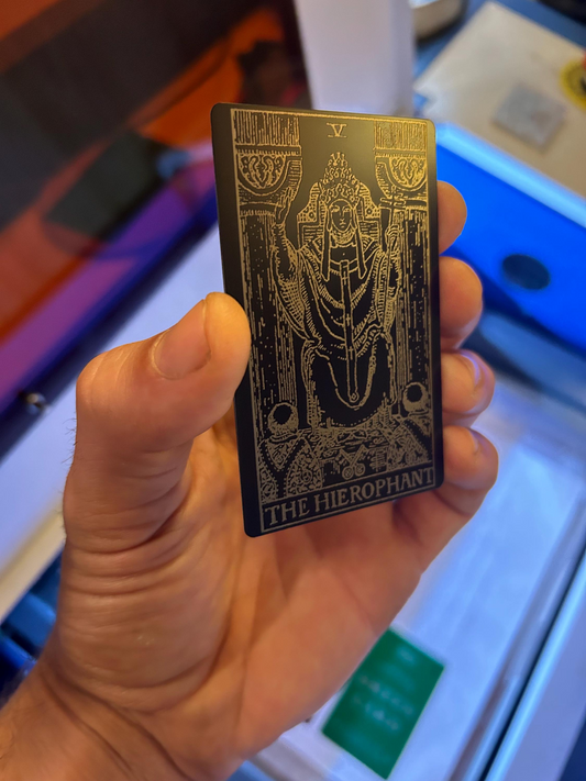Hand holding a metal The Hierophant tarot card with intricate design and text laser engraved in anodized aluminum