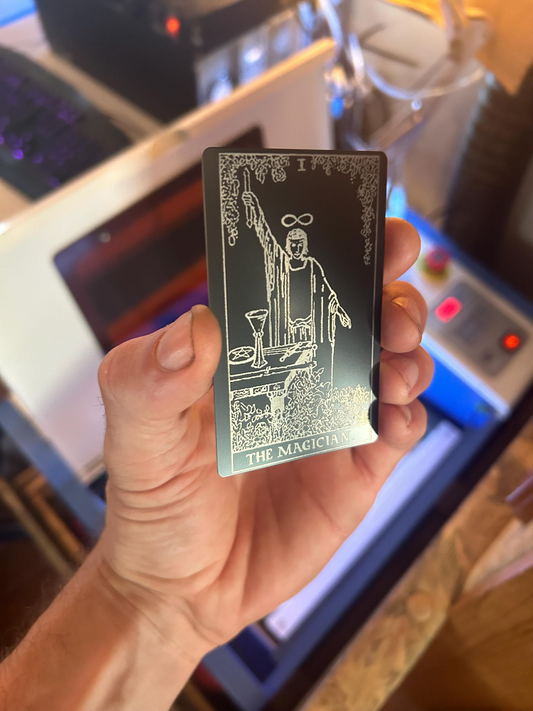 Hand holding a metal magician tarot card with intricate design against a blurred indoor background
