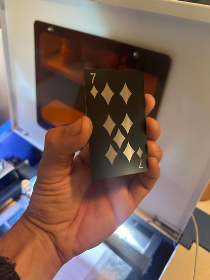 Hand holding a metal seven of diamonds playing card with laser engraved gaming design