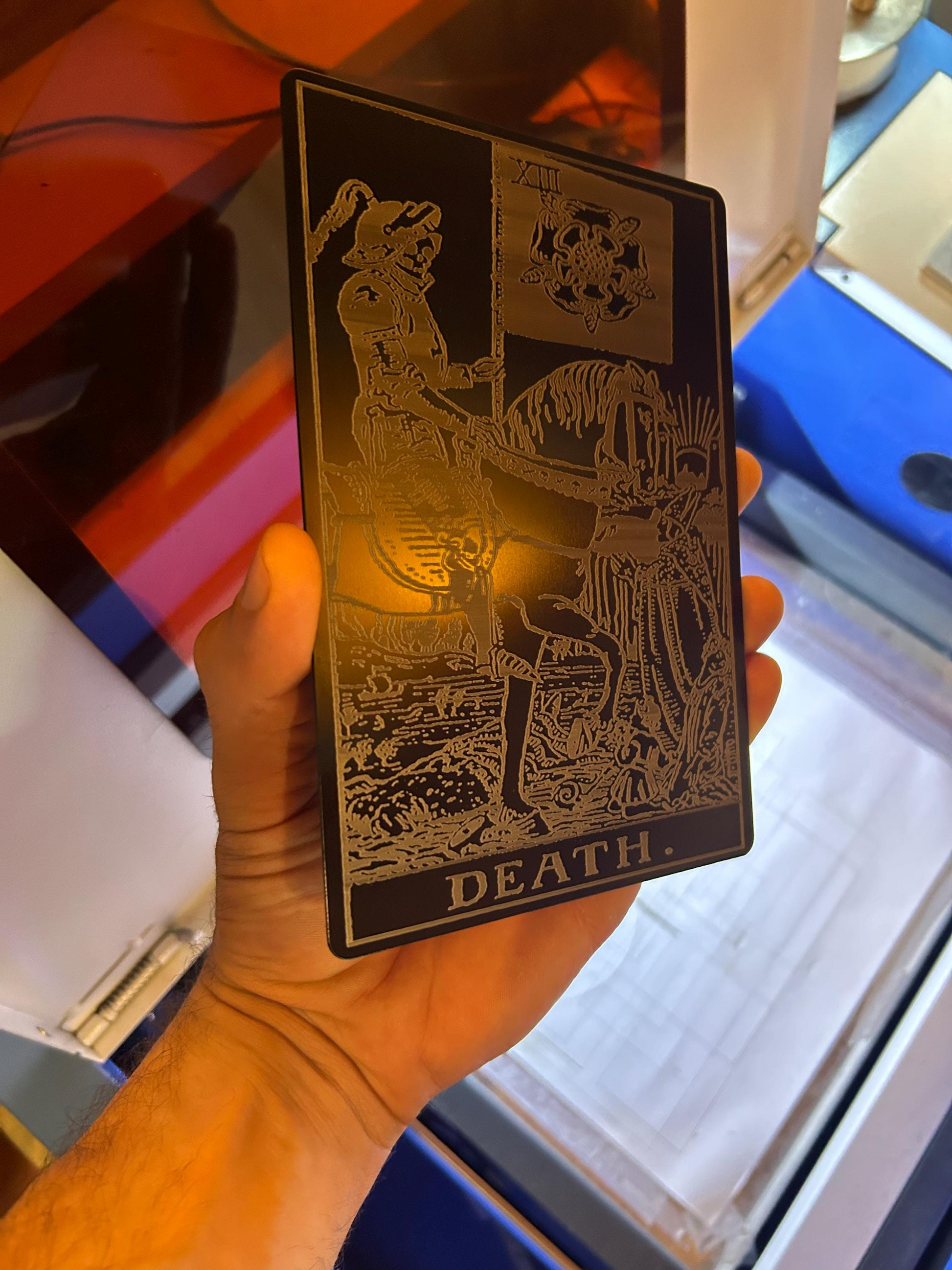 Hand holding a laser engraved metal 5x7 oversized tarot card in anodized aluminum with intricate silver design and 'DEATH' text.