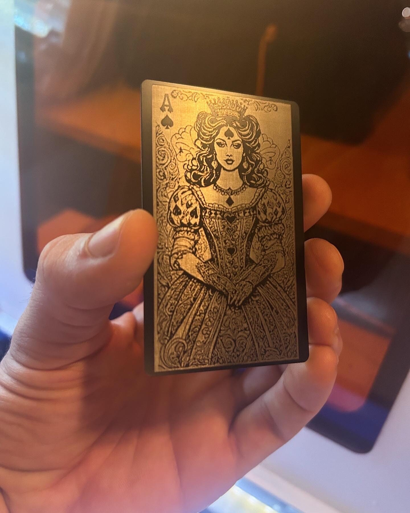 Metal black and silver playing card with a decorative Lady Luck Ace of SPades design held in a hand against a blurred background