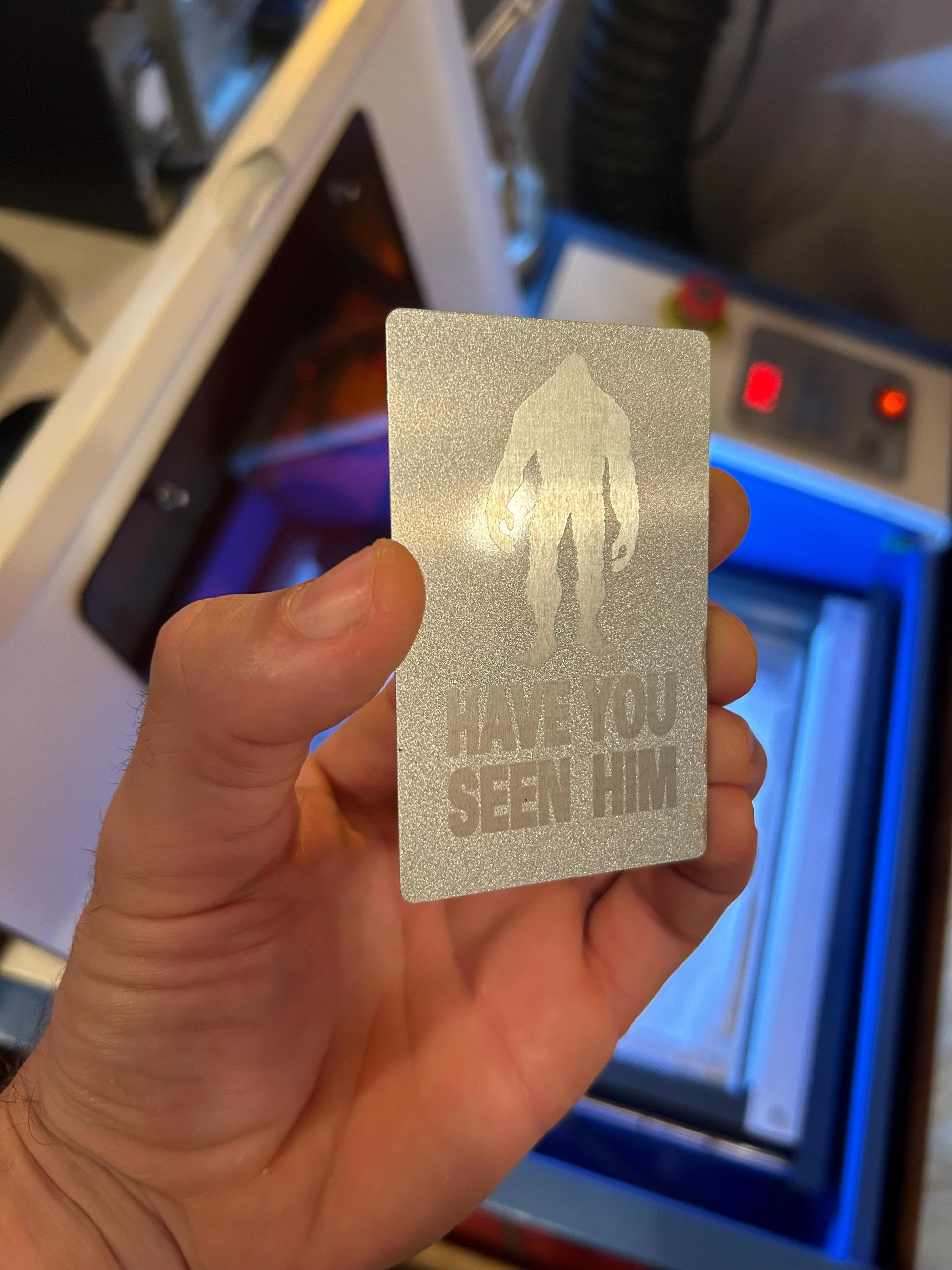 Hand holding a metallic card with sasquatch text in front of a machine.