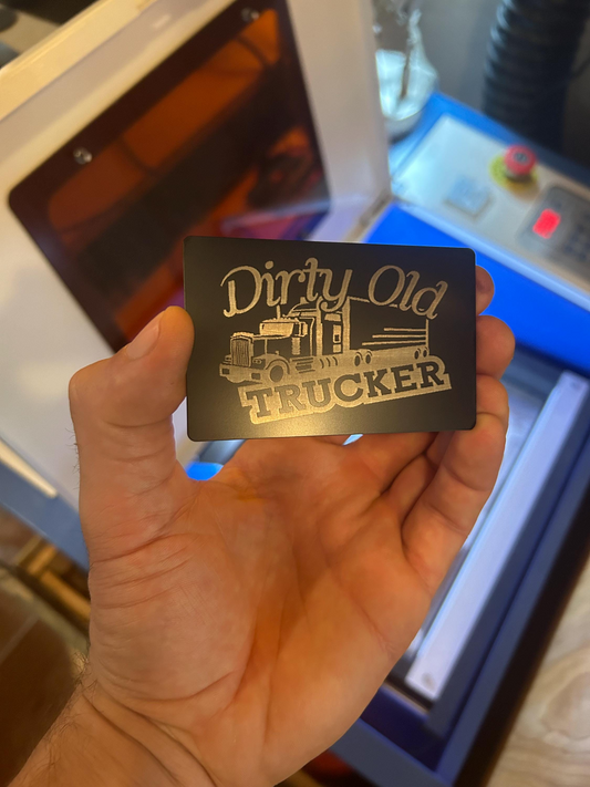 Hand holding a 'Dirty Old Trucker' card with a truck graphic in front of a machine.