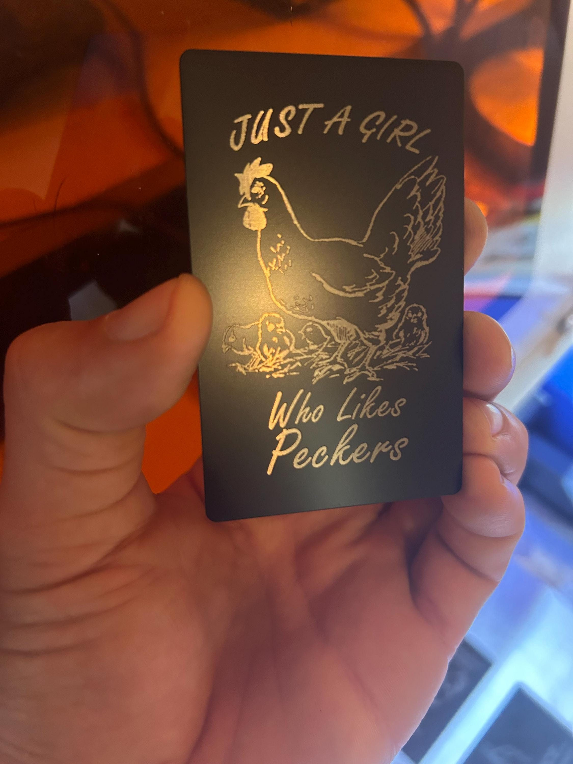 Hand presenting a novelty Friendsgiving metal card engraved with “Just A Girl Who Likes Peckers” and chicken illustration