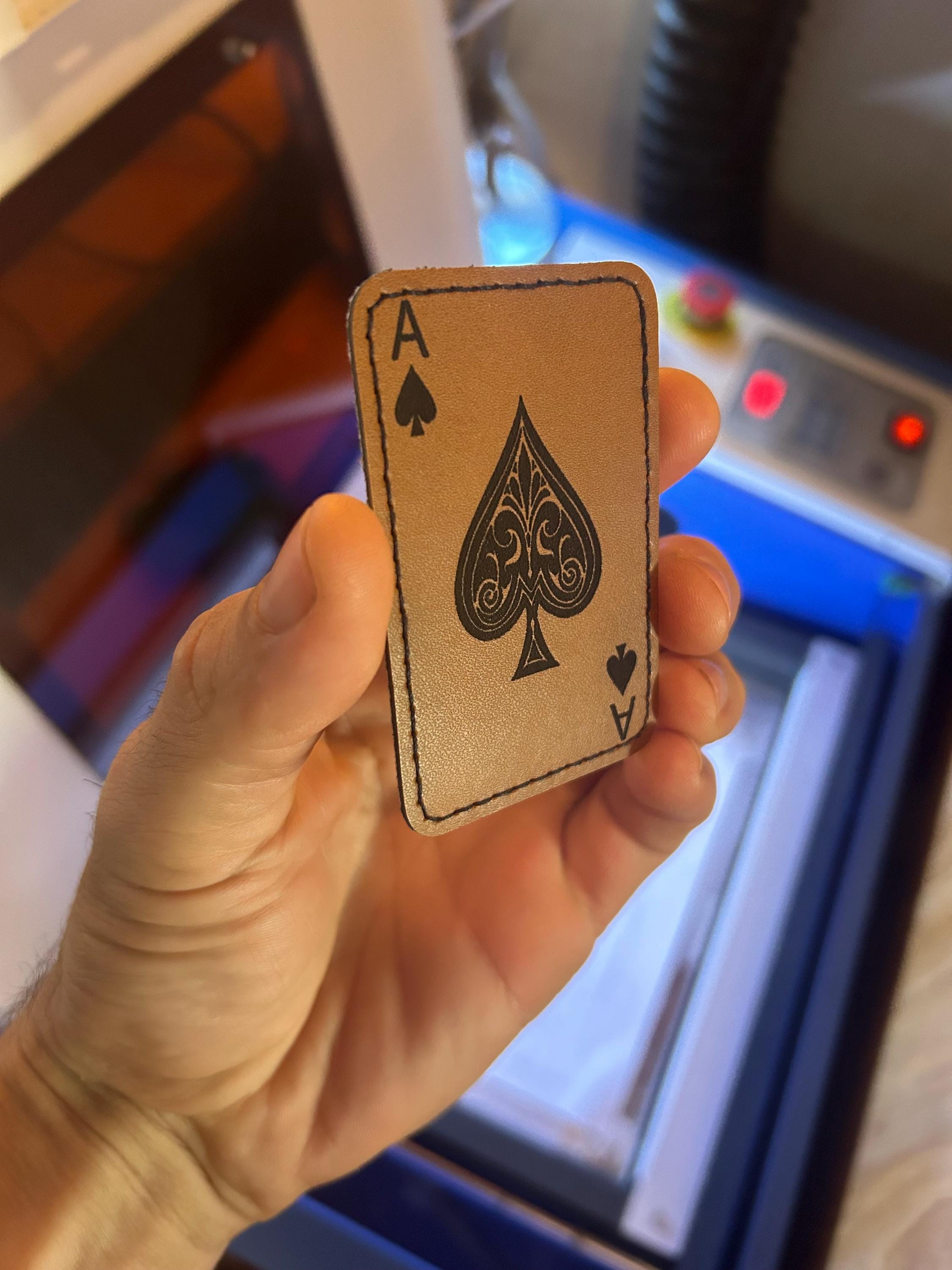 Hand holding an Ace of Spades brown leather patch in front of a machine with a blurred background