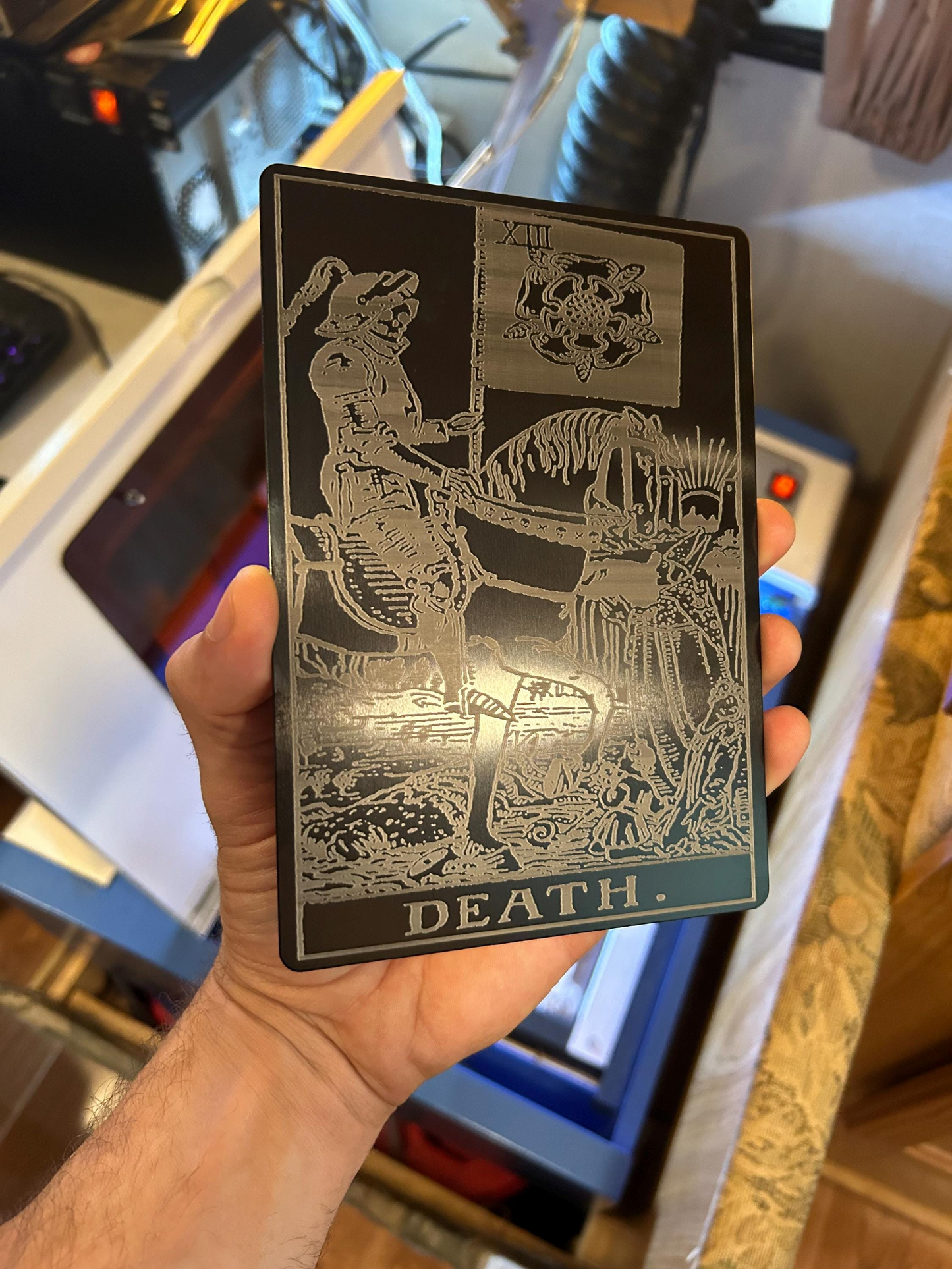 Hand holding a 5x7 metal sign with tarot card design engraved labeled 'Death' with intricate design.
