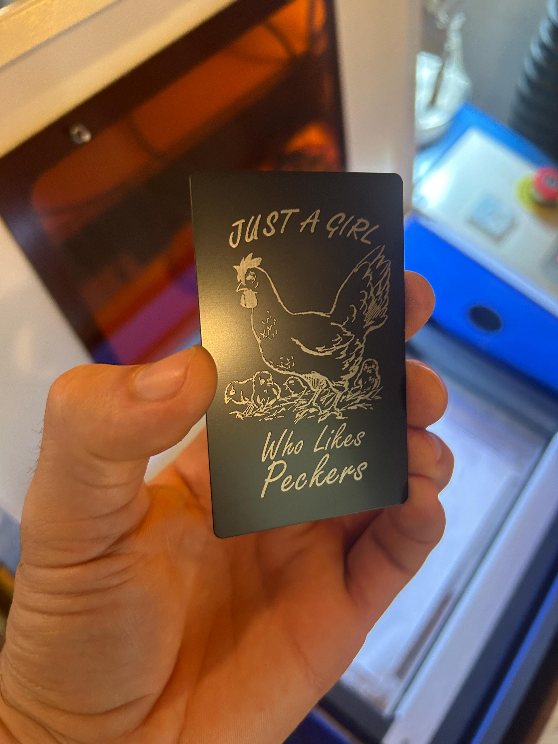 Side angle of engraved anodized aluminum gag gift card featuring “Just A Girl Who Likes Peckers” joke and chicken design