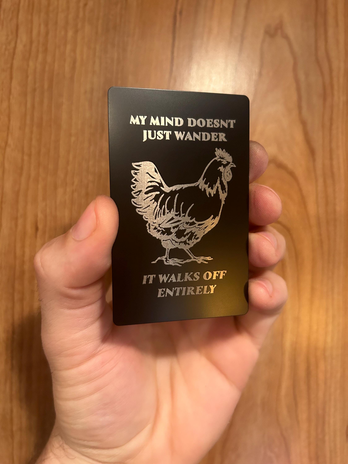 Detailed view of engraved anodized aluminum gag gift card with silly chicken design and inspirational humor quote