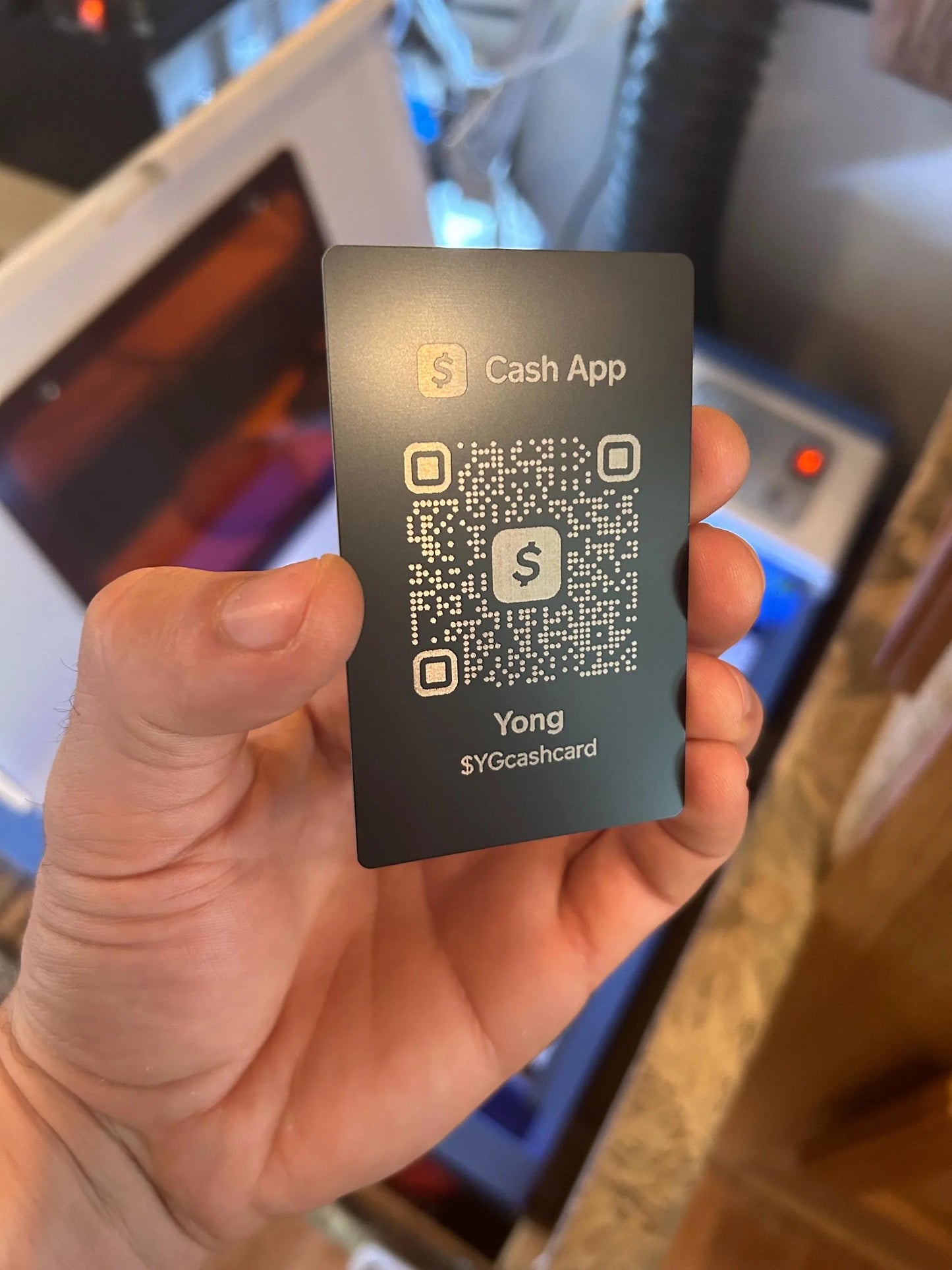 Hand holding a Cash App card with a QR code and logo.