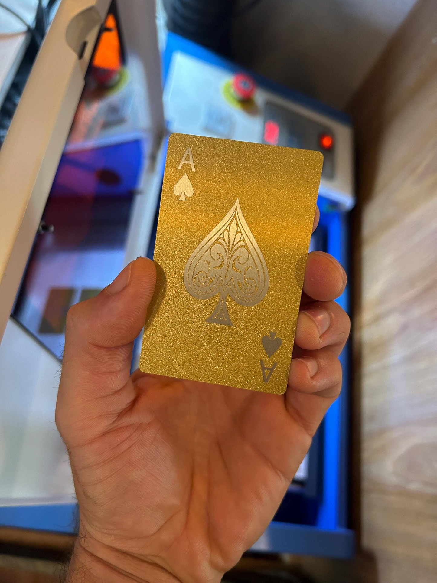 Gold/silver metal playing card with an ace of spades held by a hand in front of a blurred background