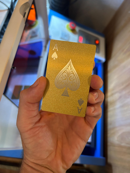 Gold/silver metal playing card with an ace of spades held by a hand in front of a blurred background